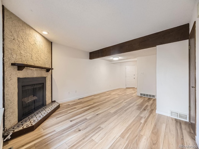 unfurnished living room featuring beamed ceiling, a large fireplace, a textured ceiling, and light hardwood / wood-style floors