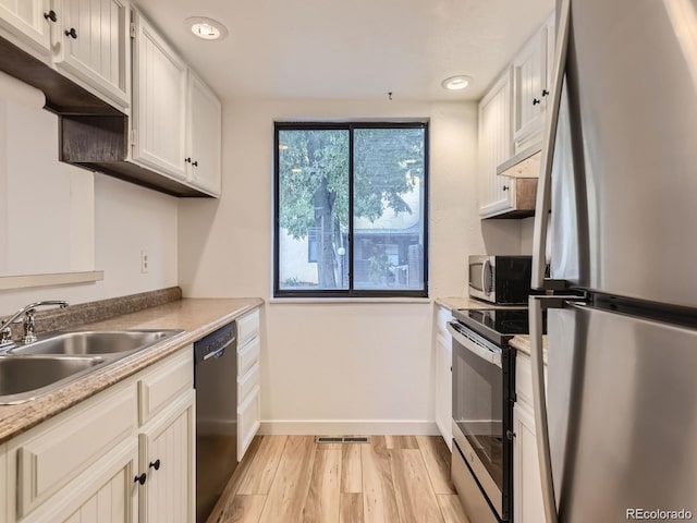 kitchen featuring appliances with stainless steel finishes, sink, white cabinets, and light hardwood / wood-style flooring