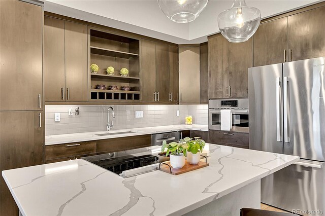 kitchen with light stone counters, appliances with stainless steel finishes, a sink, tasteful backsplash, and pendant lighting