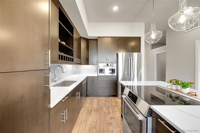 kitchen with dark brown cabinetry, light wood-style floors, a sink, appliances with stainless steel finishes, and backsplash