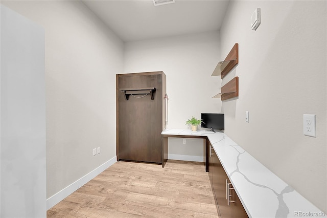 unfurnished office with light wood-type flooring, baseboards, and built in study area