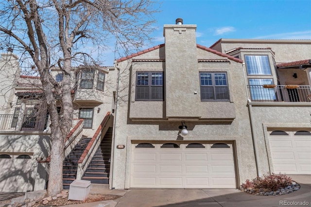 view of property featuring driveway, a chimney, an attached garage, stairs, and stucco siding