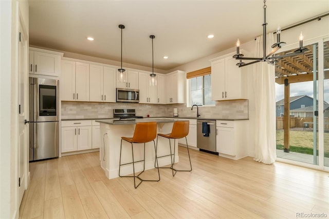 kitchen featuring white cabinets, appliances with stainless steel finishes, a center island, light wood finished floors, and tasteful backsplash