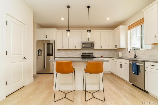 kitchen featuring light wood finished floors, a center island, stainless steel appliances, white cabinetry, and a sink