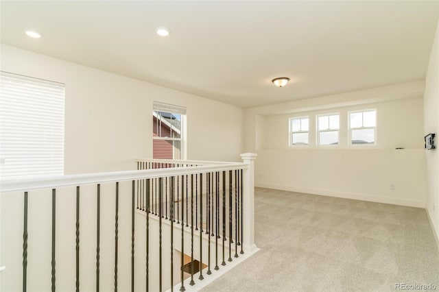 hallway with an upstairs landing, light colored carpet, plenty of natural light, and baseboards