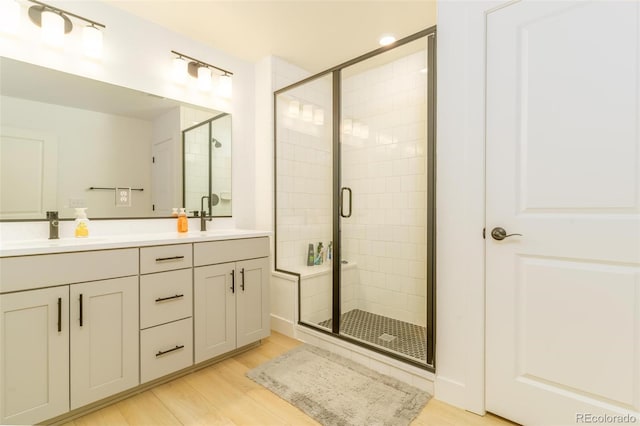 full bathroom featuring double vanity, wood finished floors, a sink, and a shower stall