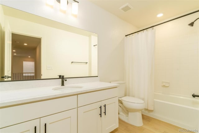 bathroom featuring visible vents, toilet, wood finished floors, shower / bath combo with shower curtain, and vanity