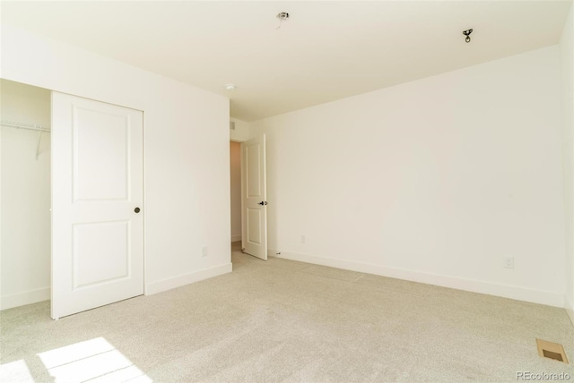 unfurnished bedroom featuring visible vents, baseboards, a closet, and light colored carpet