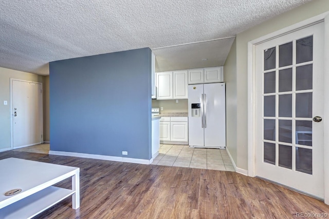 kitchen featuring white fridge with ice dispenser, white cabinets, a textured ceiling, and light wood-type flooring