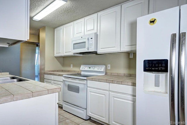 kitchen featuring sink, white appliances, light tile patterned floors, white cabinetry, and tile countertops