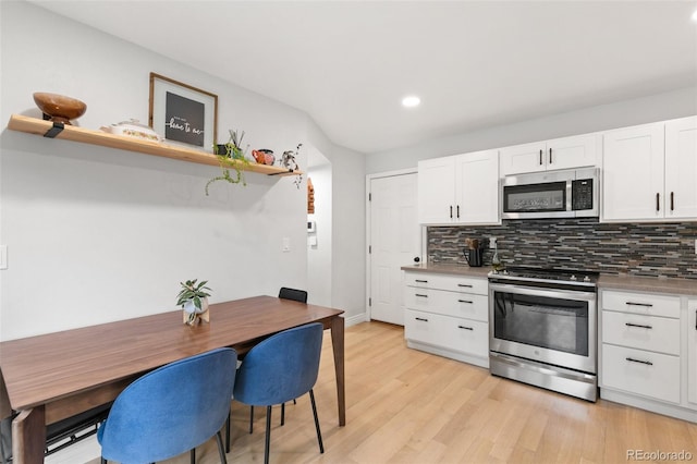 kitchen with white cabinets, backsplash, appliances with stainless steel finishes, and light hardwood / wood-style flooring