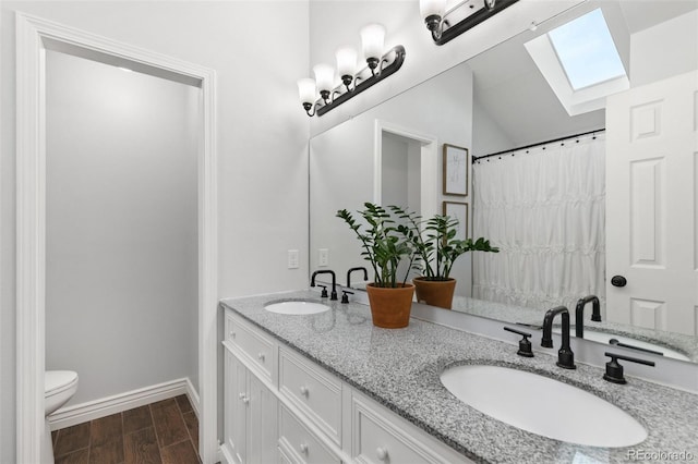 bathroom with toilet, hardwood / wood-style floors, vanity, and lofted ceiling with skylight