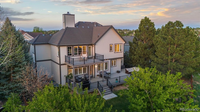 7071 Turweston Ln, Castle Pines, CO 80108 - back of house at dusk featuring a balcony, an outdoor living space, a chimney, a shingled roof, and outdoor dining space