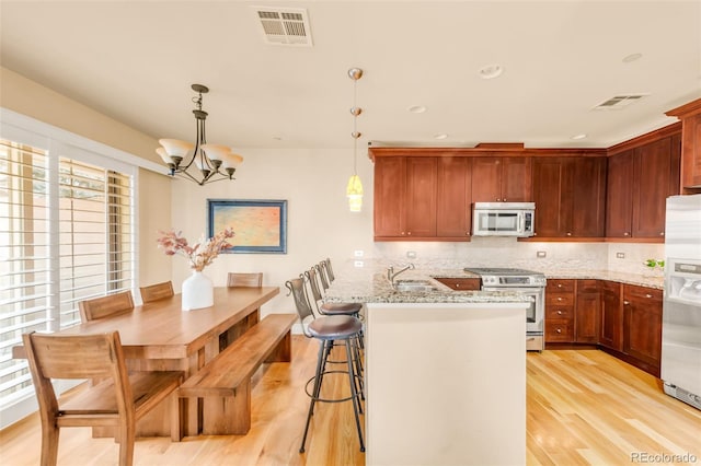 kitchen with kitchen peninsula, light hardwood / wood-style flooring, hanging light fixtures, a wealth of natural light, and stainless steel appliances