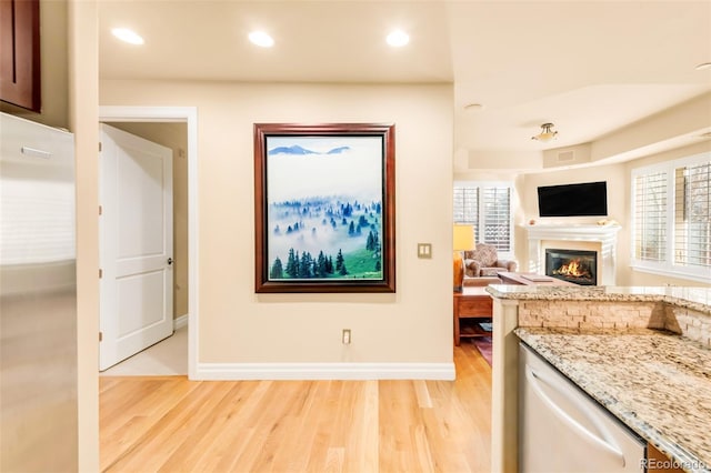 kitchen featuring light hardwood / wood-style flooring, dishwasher, light stone countertops, and stainless steel refrigerator