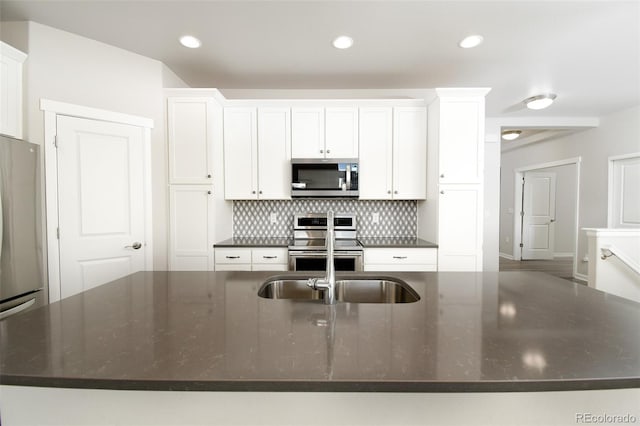 kitchen with white cabinets, dark stone countertops, an island with sink, tasteful backsplash, and stainless steel appliances