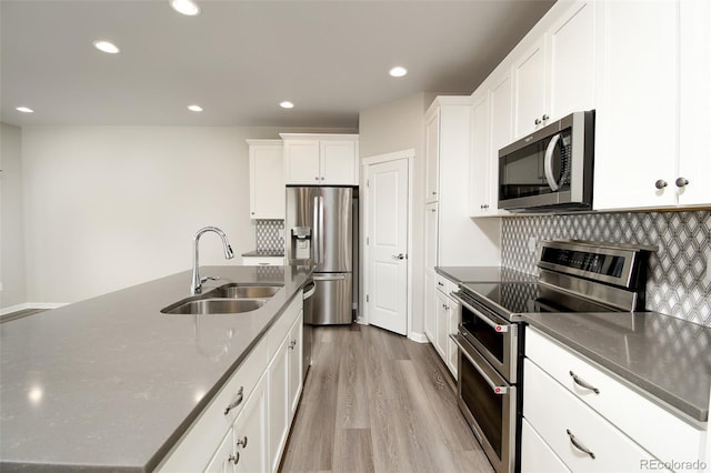 kitchen with appliances with stainless steel finishes, white cabinetry, a kitchen island with sink, and sink