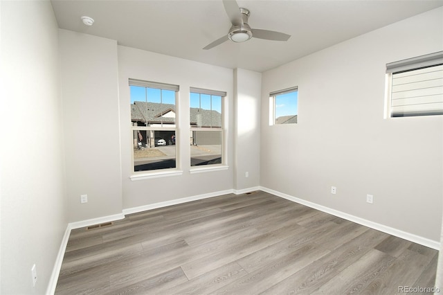 empty room with a wealth of natural light, hardwood / wood-style flooring, and ceiling fan