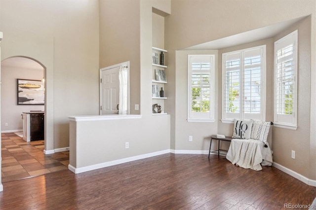 living area with arched walkways, a towering ceiling, wood finished floors, and plenty of natural light