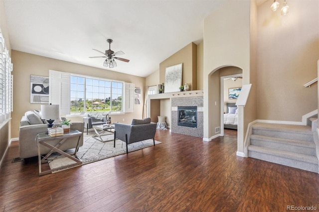 living area with ceiling fan, arched walkways, wood finished floors, baseboards, and high vaulted ceiling