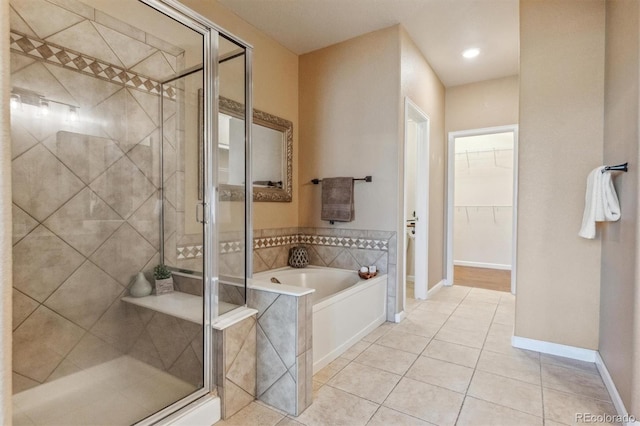 full bath featuring a stall shower, tile patterned flooring, a bath, a walk in closet, and baseboards