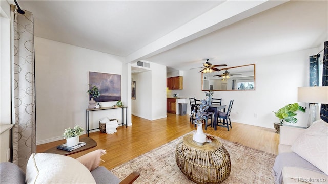 living area with light wood-style floors, baseboards, visible vents, and beam ceiling