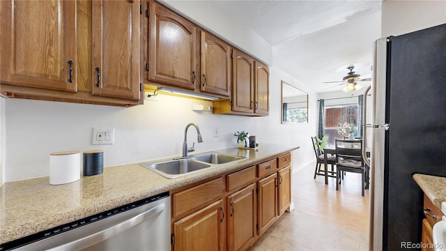 kitchen with brown cabinets, appliances with stainless steel finishes, a sink, ceiling fan, and light stone countertops