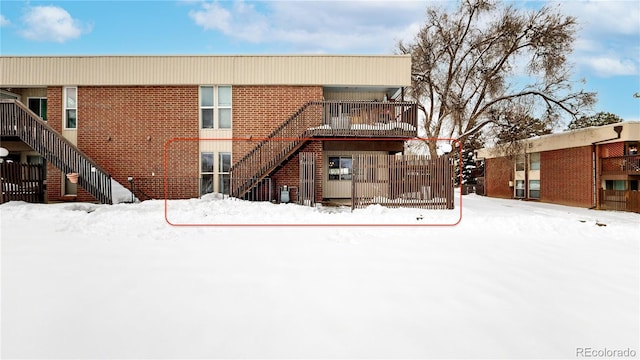 snow covered rear of property featuring brick siding, stairway, and a balcony