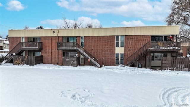 snow covered property featuring stairs and brick siding