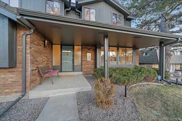 property entrance with board and batten siding, covered porch, and brick siding