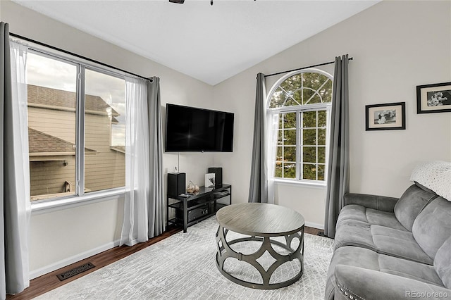 living area featuring lofted ceiling, visible vents, baseboards, and wood finished floors