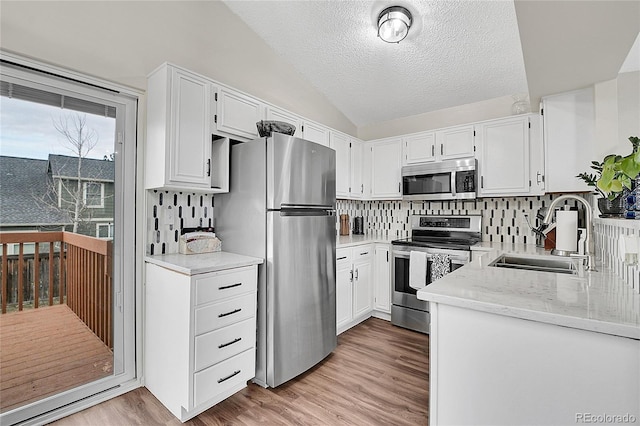 kitchen featuring lofted ceiling, light wood-style flooring, stainless steel appliances, white cabinetry, and a sink