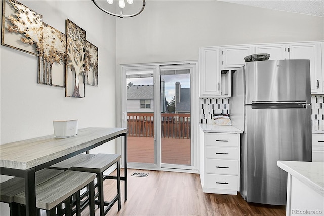 kitchen featuring visible vents, white cabinets, light stone counters, wood finished floors, and freestanding refrigerator