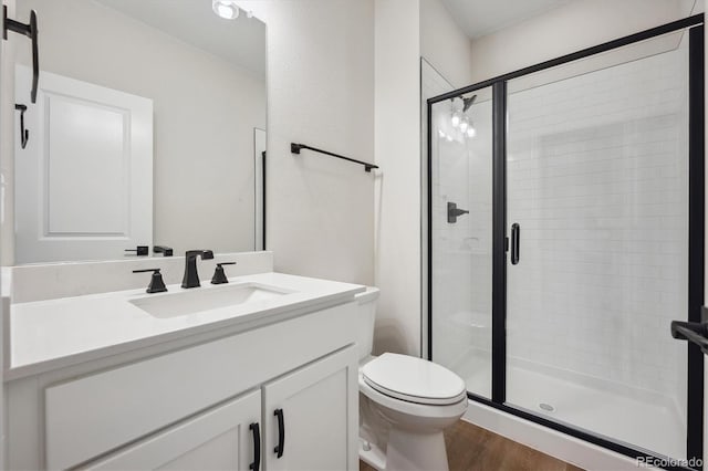 bathroom featuring vanity, toilet, wood finished floors, and a stall shower