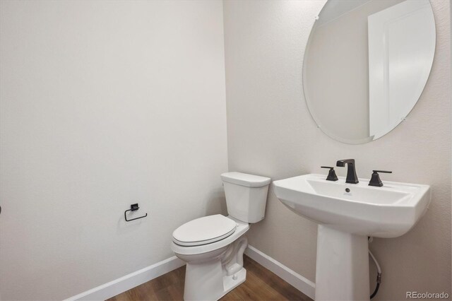 half bathroom with baseboards, toilet, and wood finished floors