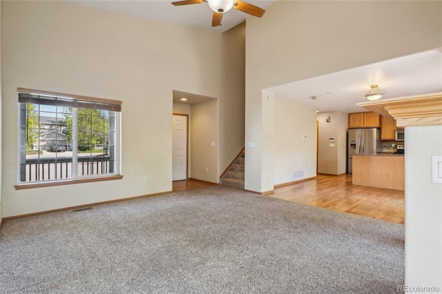 1481 Box Prairie Cir, Loveland, CO 80538 - unfurnished living room with light colored carpet, stairway, a towering ceiling, a ceiling fan, and baseboards