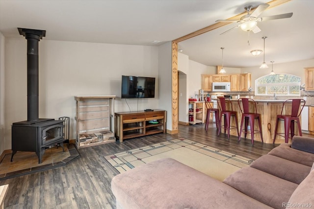 living area with baseboards, a wood stove, ceiling fan, and dark wood-style floors