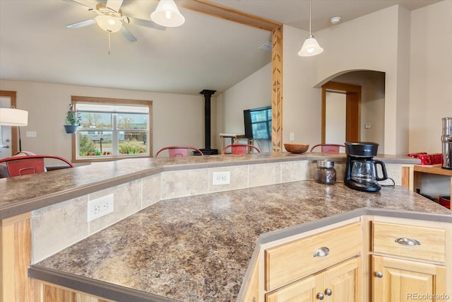 kitchen featuring a wood stove, light brown cabinets, arched walkways, a ceiling fan, and vaulted ceiling