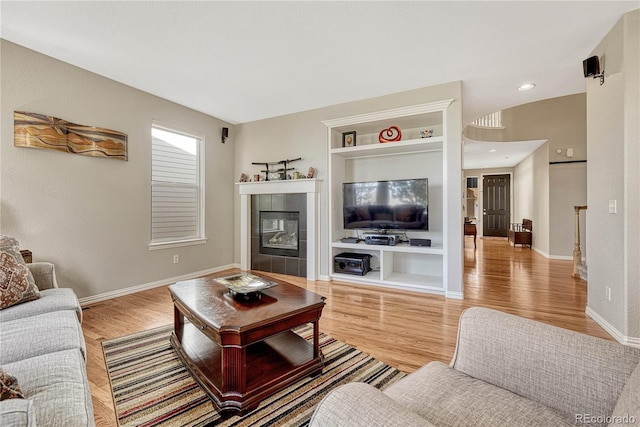 living room featuring built in shelves, light wood-type flooring, and a tile fireplace