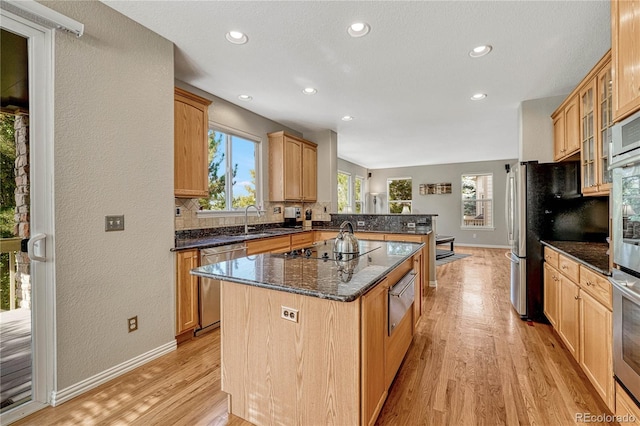 kitchen featuring a kitchen island, appliances with stainless steel finishes, sink, light hardwood / wood-style floors, and dark stone countertops