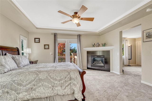 bedroom with ceiling fan, access to exterior, a tray ceiling, a fireplace, and light colored carpet