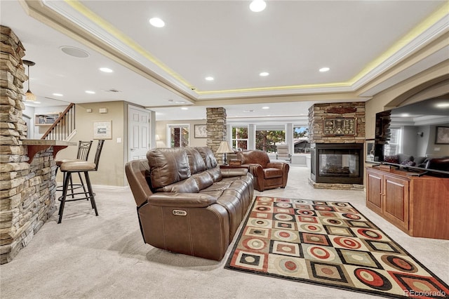 carpeted living room featuring a stone fireplace, ornamental molding, and a tray ceiling