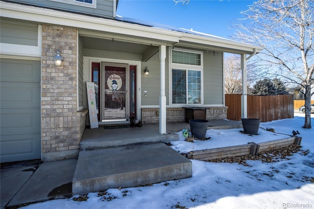 snow covered property entrance with a garage and a porch