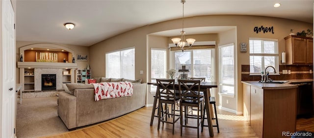 living room featuring a tile fireplace, sink, a notable chandelier, light hardwood / wood-style floors, and built in shelves