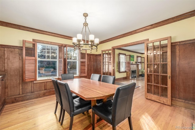 dining room with french doors, light hardwood / wood-style flooring, a chandelier, wooden walls, and ornamental molding