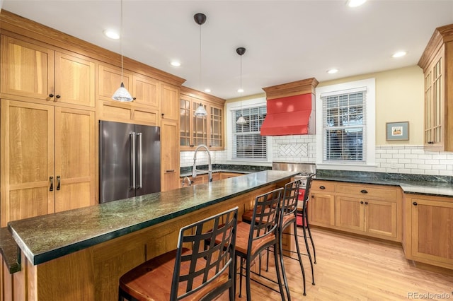 kitchen featuring backsplash, high quality fridge, a breakfast bar, decorative light fixtures, and light hardwood / wood-style floors