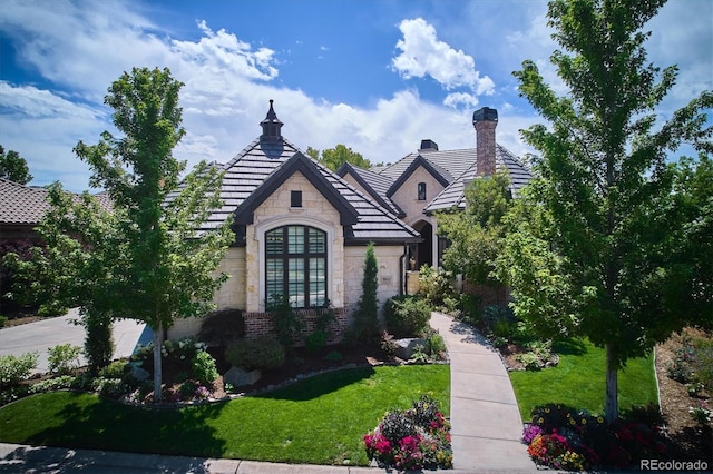 view of front of home with stone siding, brick siding, a chimney, and a front yard