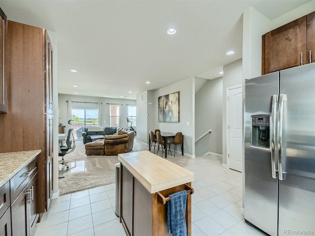 kitchen with light tile patterned flooring, stainless steel fridge, and light stone counters