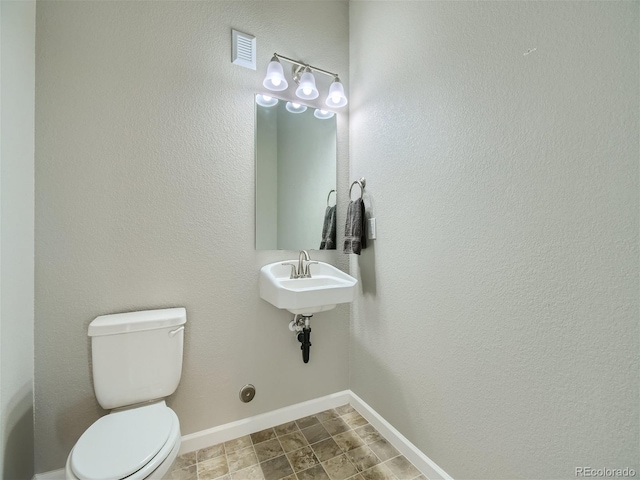 half bath with toilet, baseboards, and visible vents