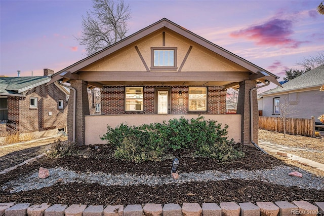 bungalow featuring brick siding, fence, and stucco siding